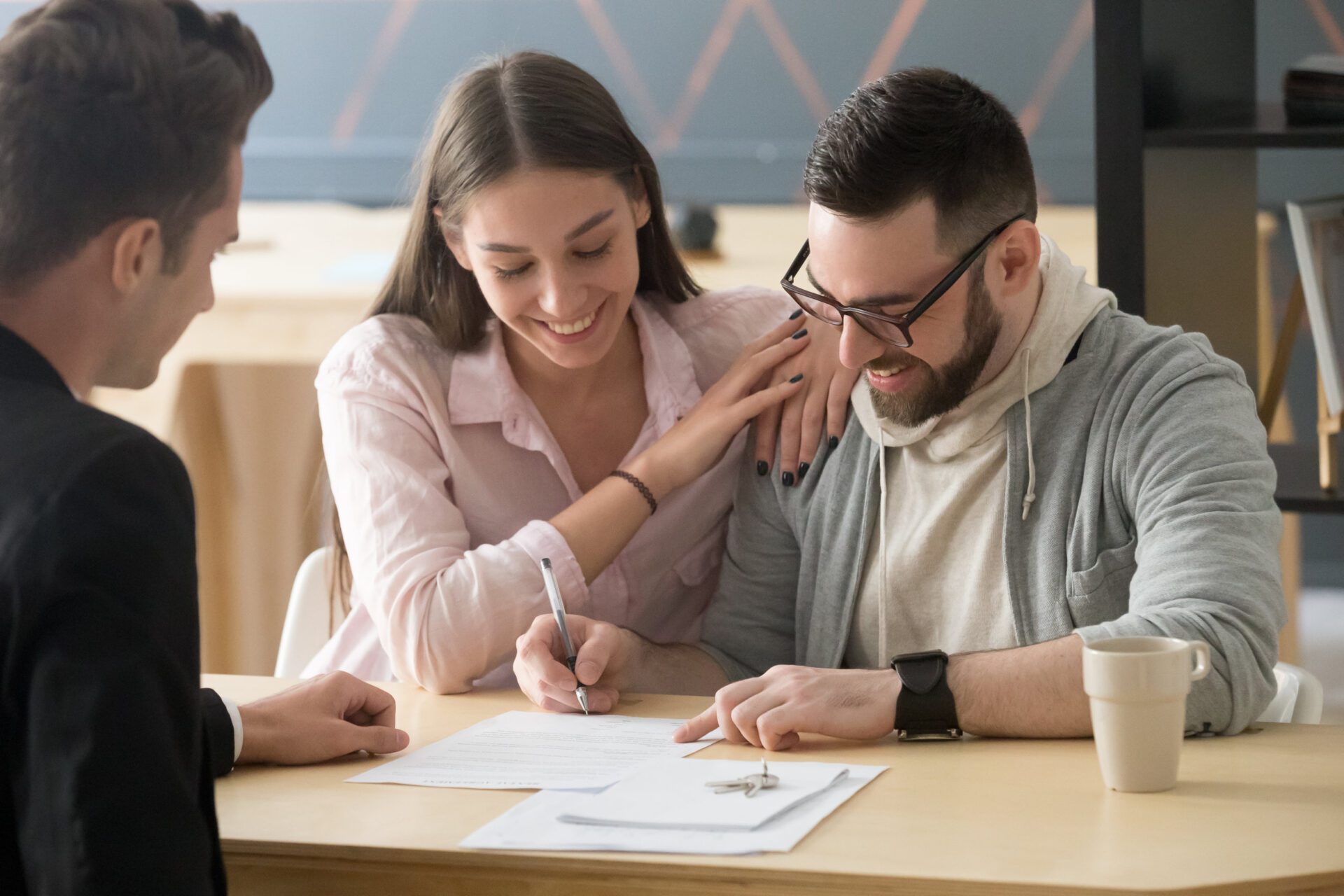 Excited couple sign purchase contract in realtor office Excited millennial couple signing purchase agreement buying first home together, husband puts signature on document, becoming apartment owner, spouses legalize property ownership in realtor office