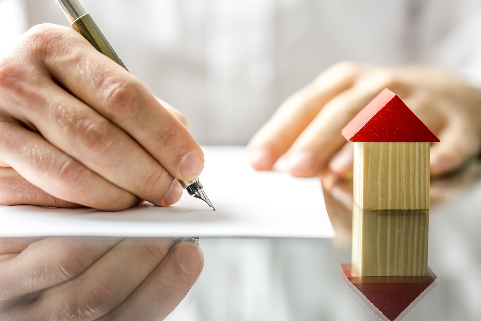 Man signing a contract when buying a new house Conceptual image of a man signing a mortgage or insurance contract or the deed of sale when buying a new house or selling his existing one with a small wooden model of a house alongside